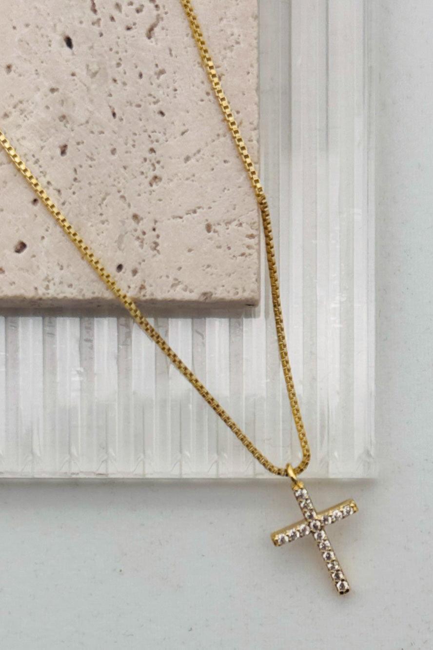 Gold necklace with a cross pendant on a light background