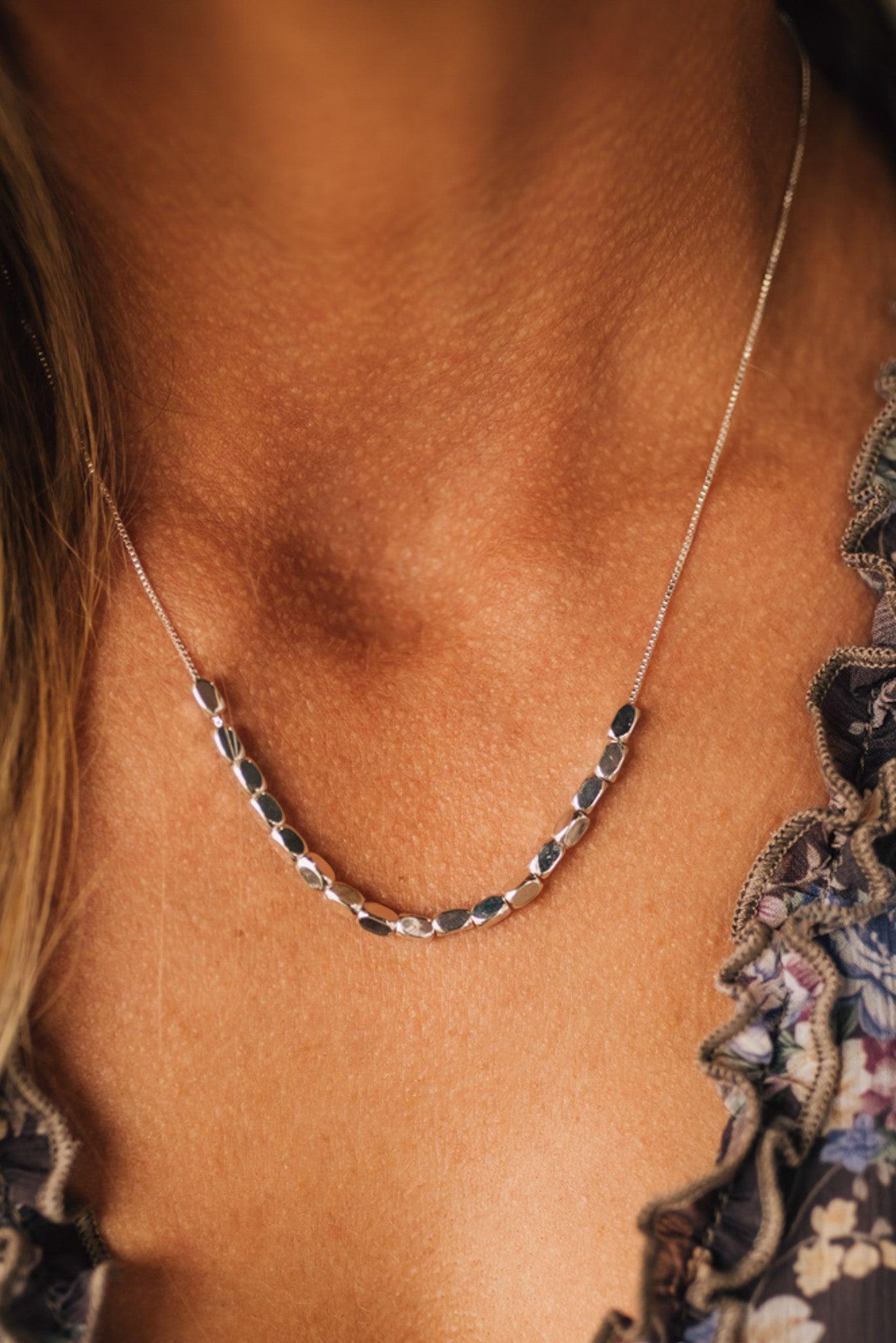 Close-up of a necklace on a person's neck with a floral garment partially visible.