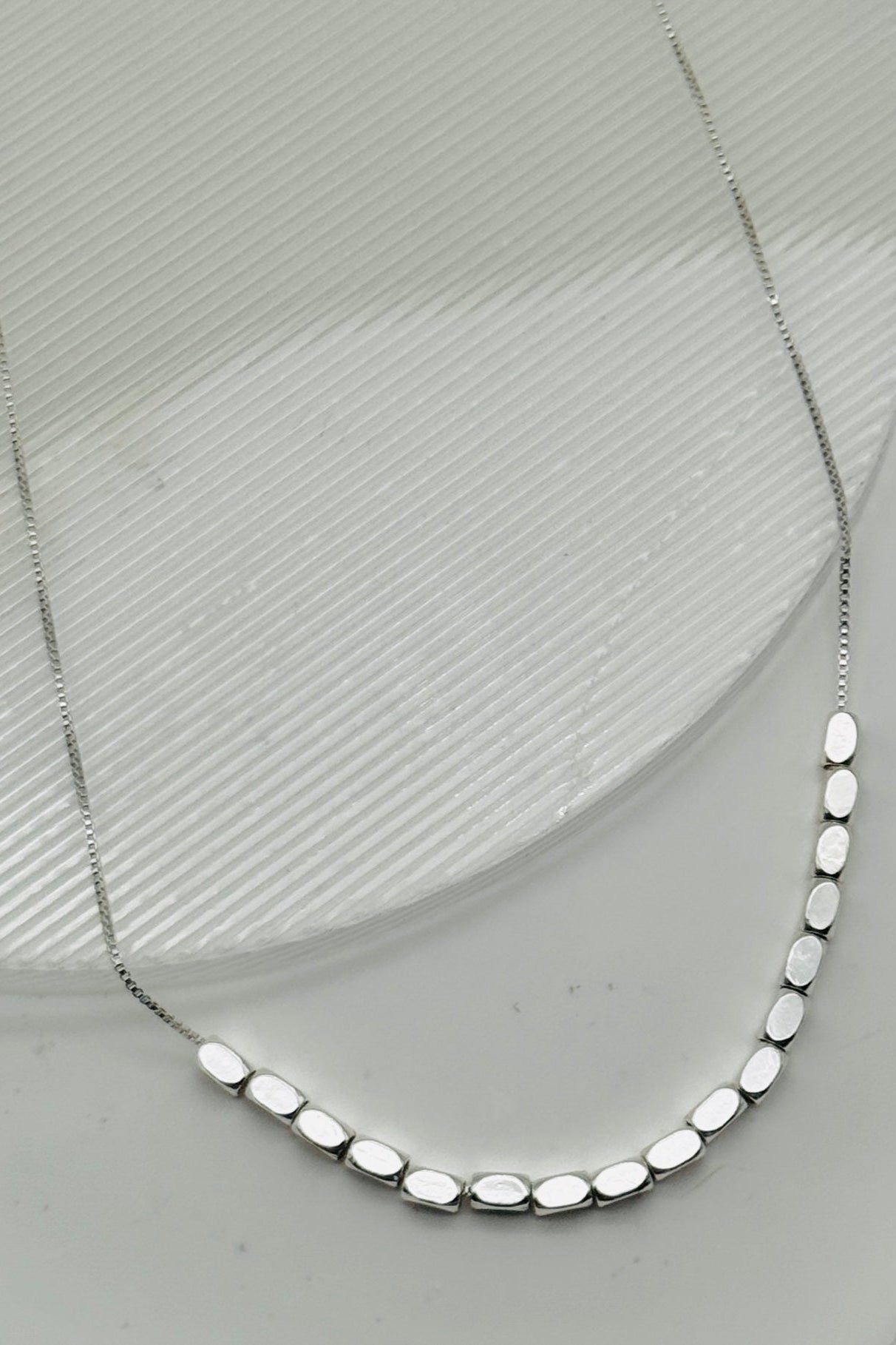 Silver necklace with oval beads on a light gray background