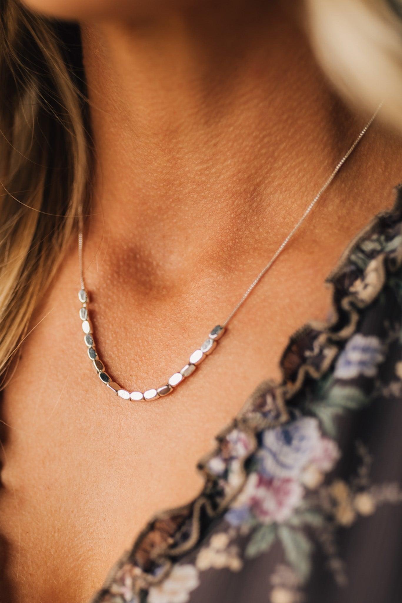 Necklace with small beads on a person wearing a floral top.