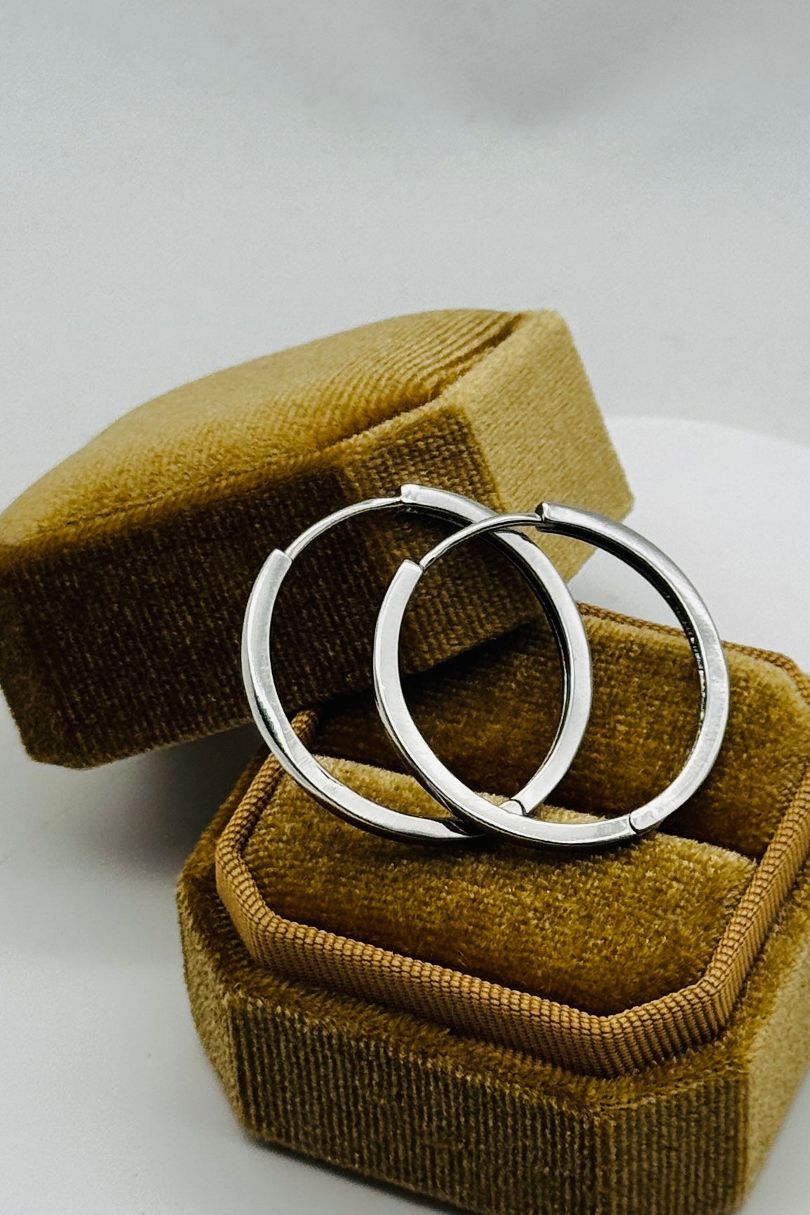 Two silver hoop earrings in a brown velvet jewelry box on a white background