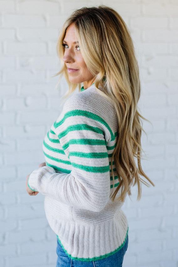 Woman wearing a white sweater with green stripes against a white background