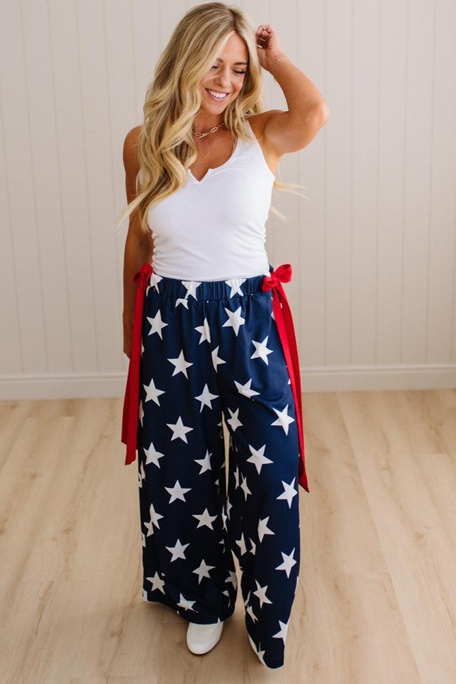 Woman wearing a white tank top and blue pants with star pattern indoors.