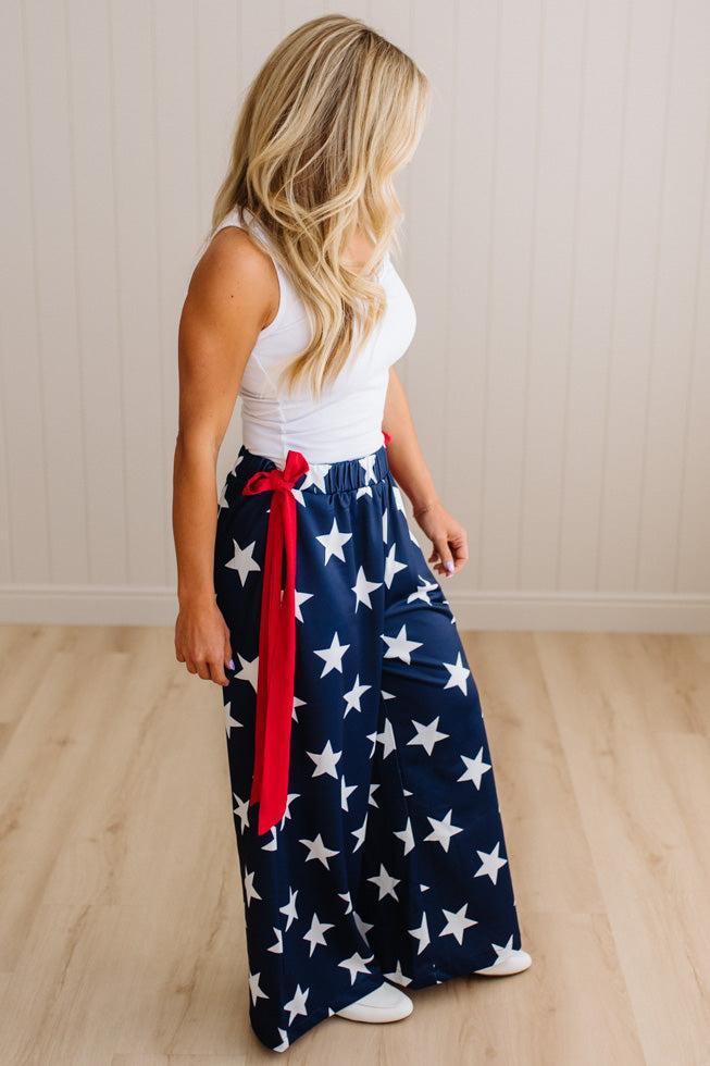 Woman wearing a white top and blue star-patterned pants with a red ribbon, standing on a wooden floor.