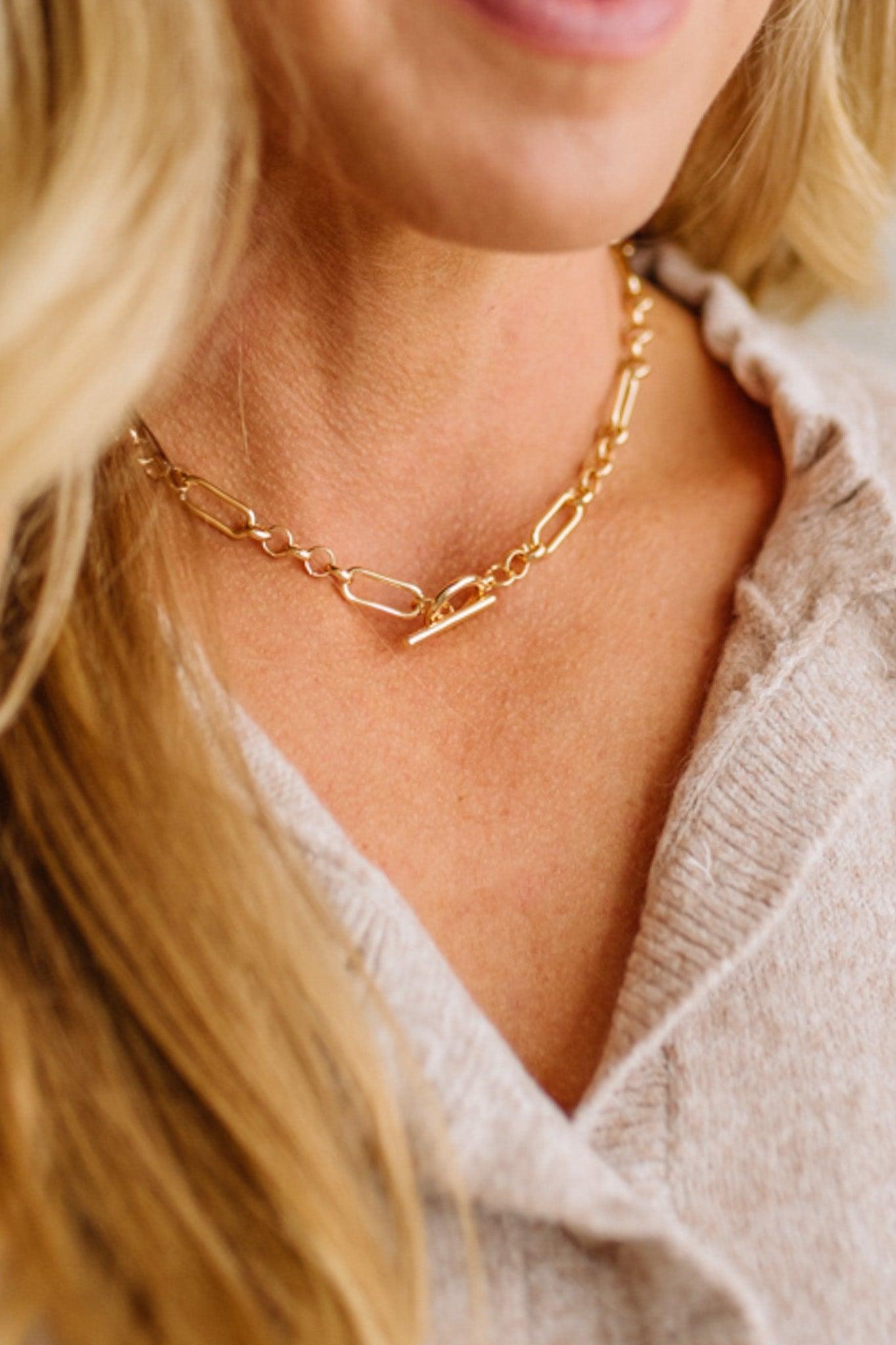 Close-up of a person wearing a gold chain necklace with a neutral background