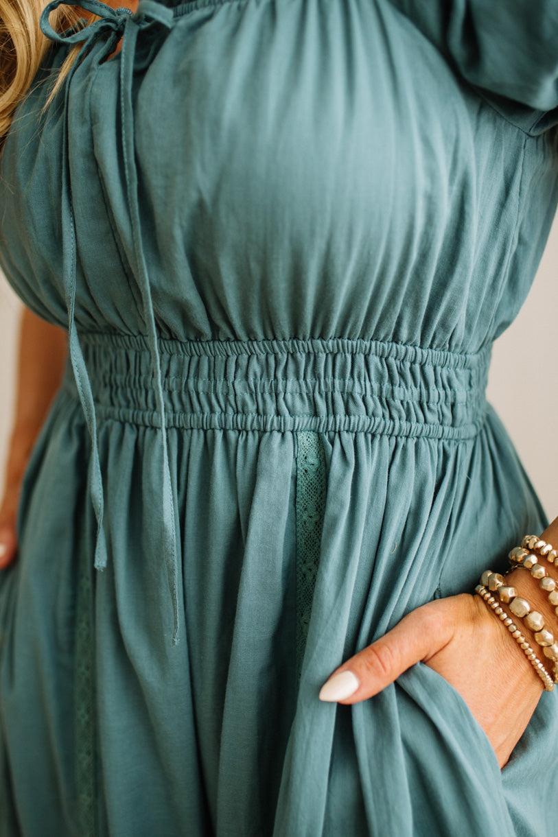 Teal dress with long sleeves and a drawstring detail on a neutral background