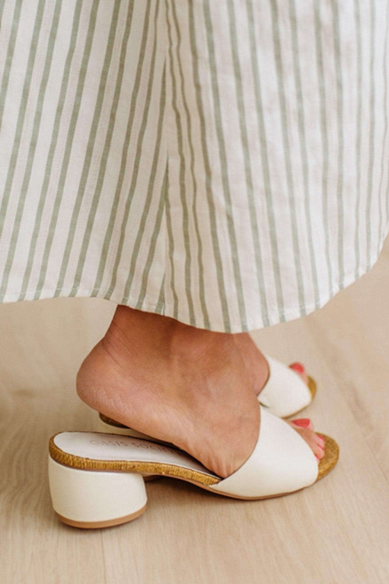 White open-toe shoes worn with a striped skirt on a neutral background