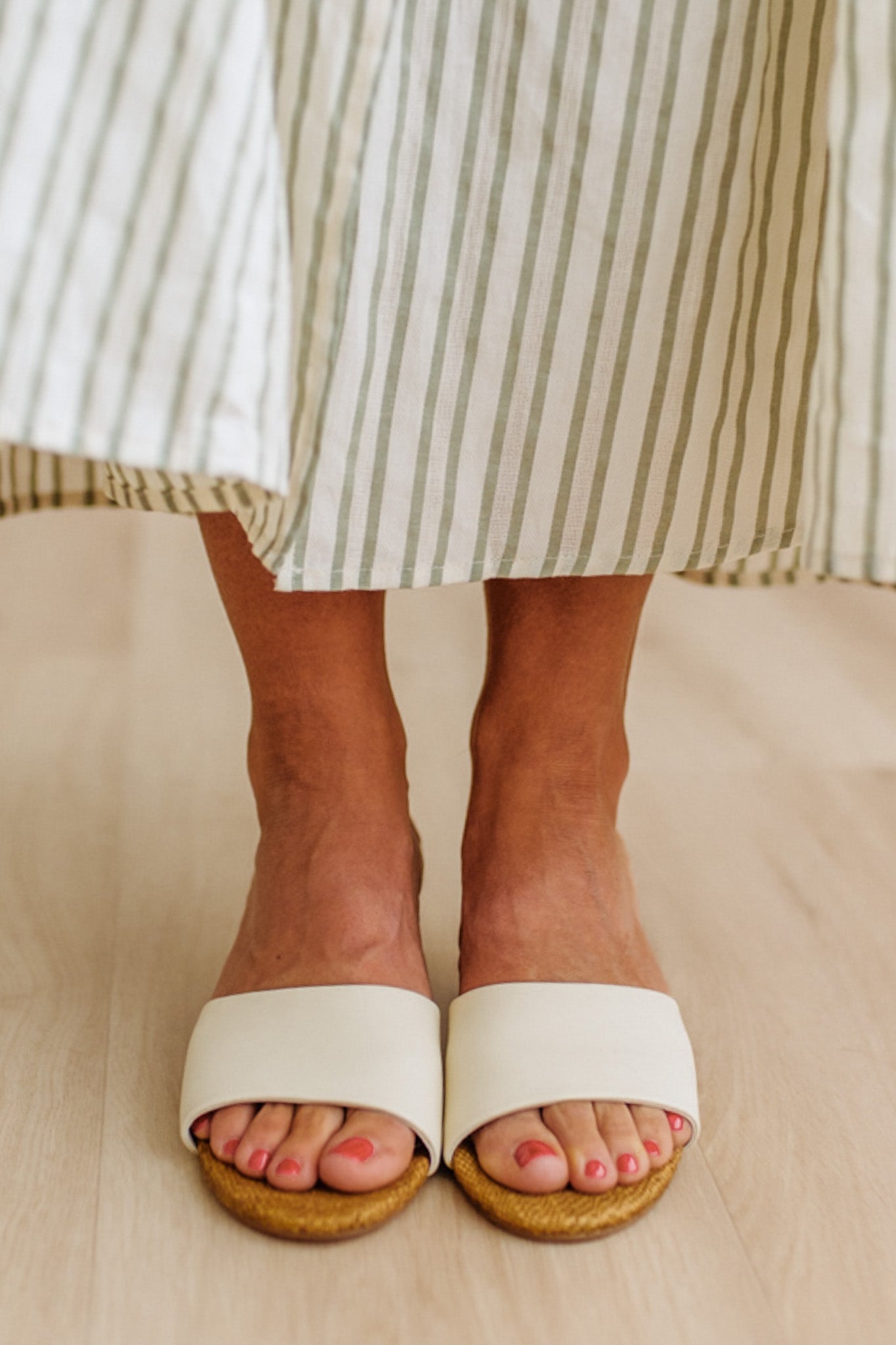 White sandals with raffia soles worn by a person in a striped skirt.