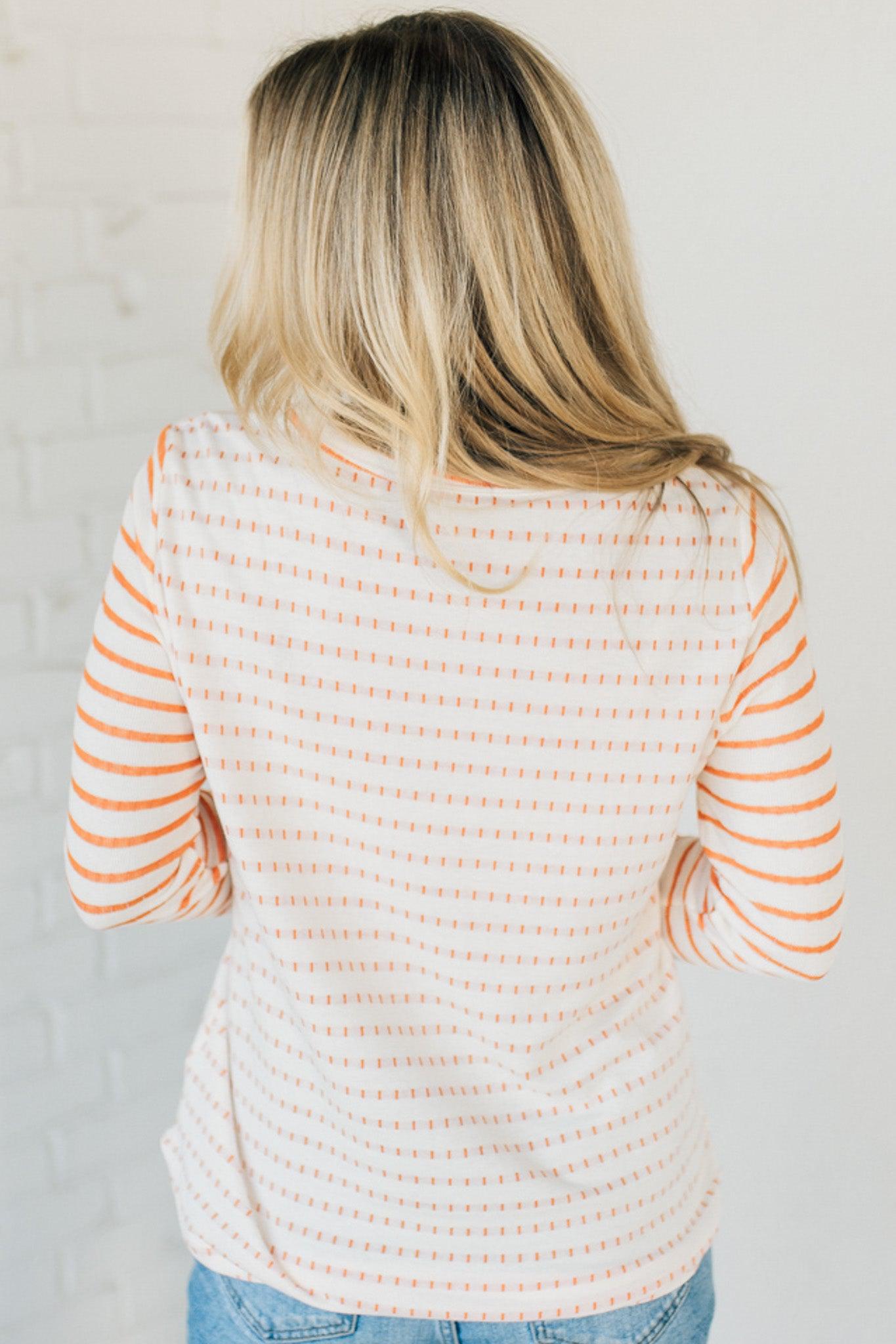 Woman wearing a striped sweater and blue jeans against a white brick wall.