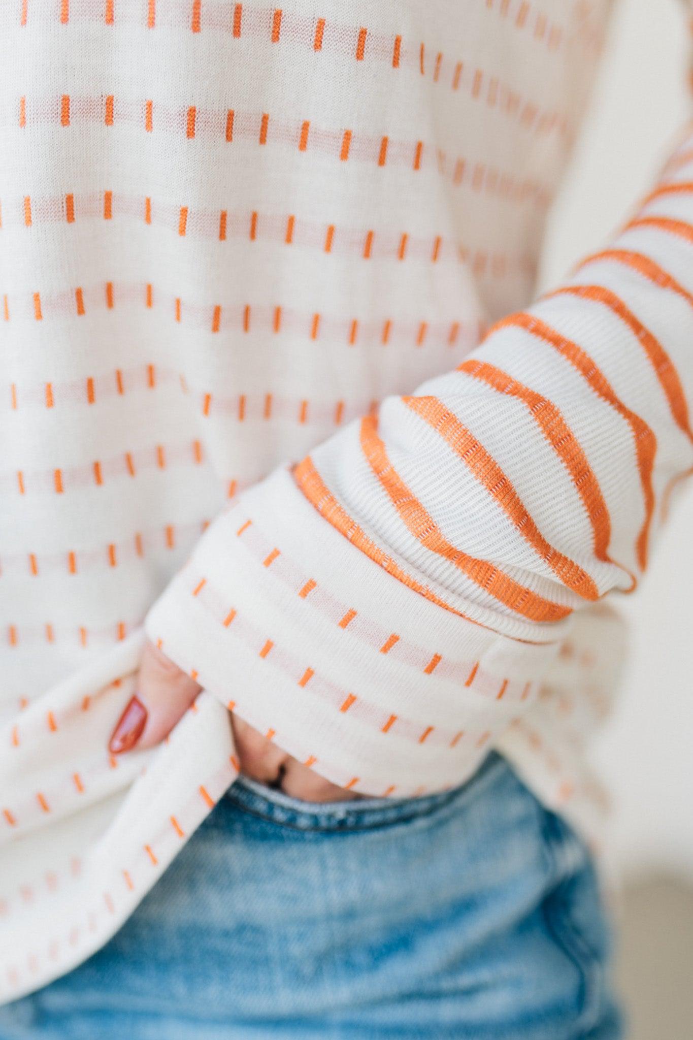 Woman wearing a striped sweater and blue jeans against a white brick wall.