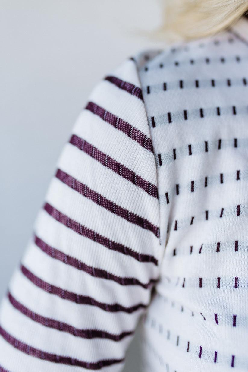 Close-up of a sweater with striped and patterned sleeves against a neutral background