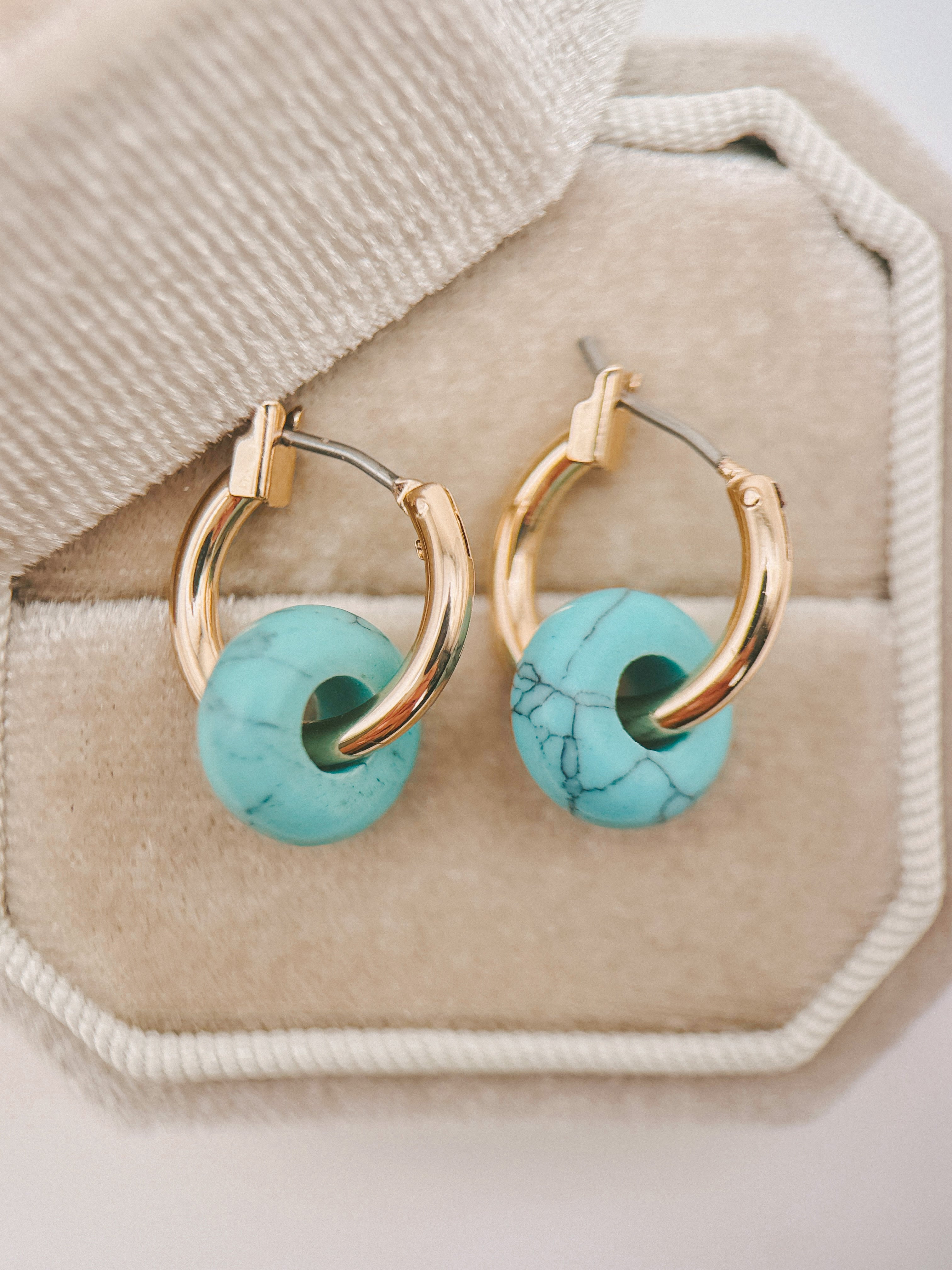 Gold hoop earrings with round turquoise beads, displayed on a beige jewelry box.