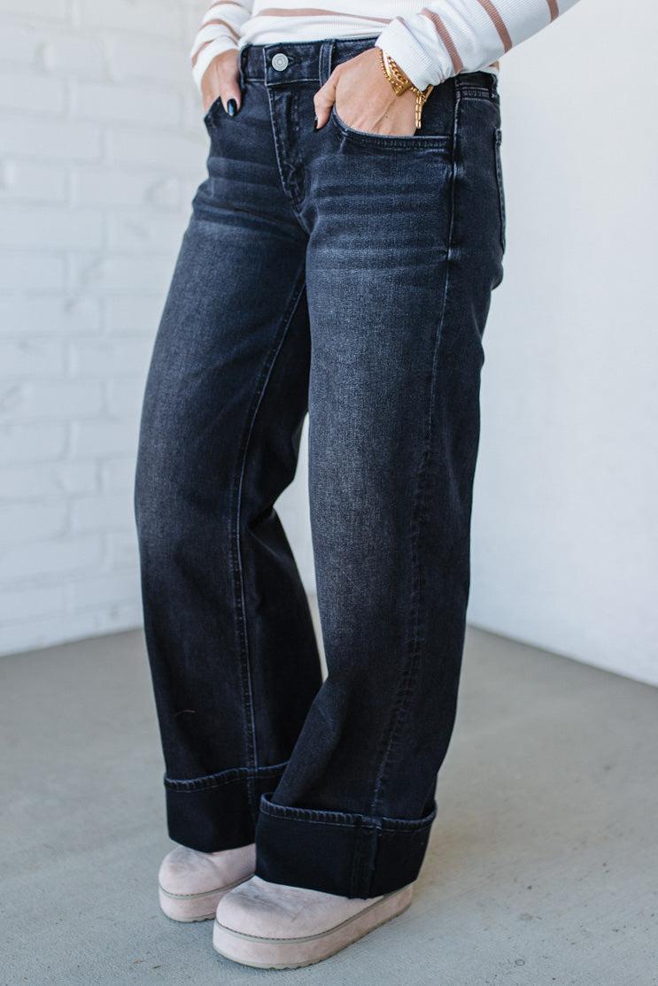 Person wearing dark blue jeans with a white brick wall background
