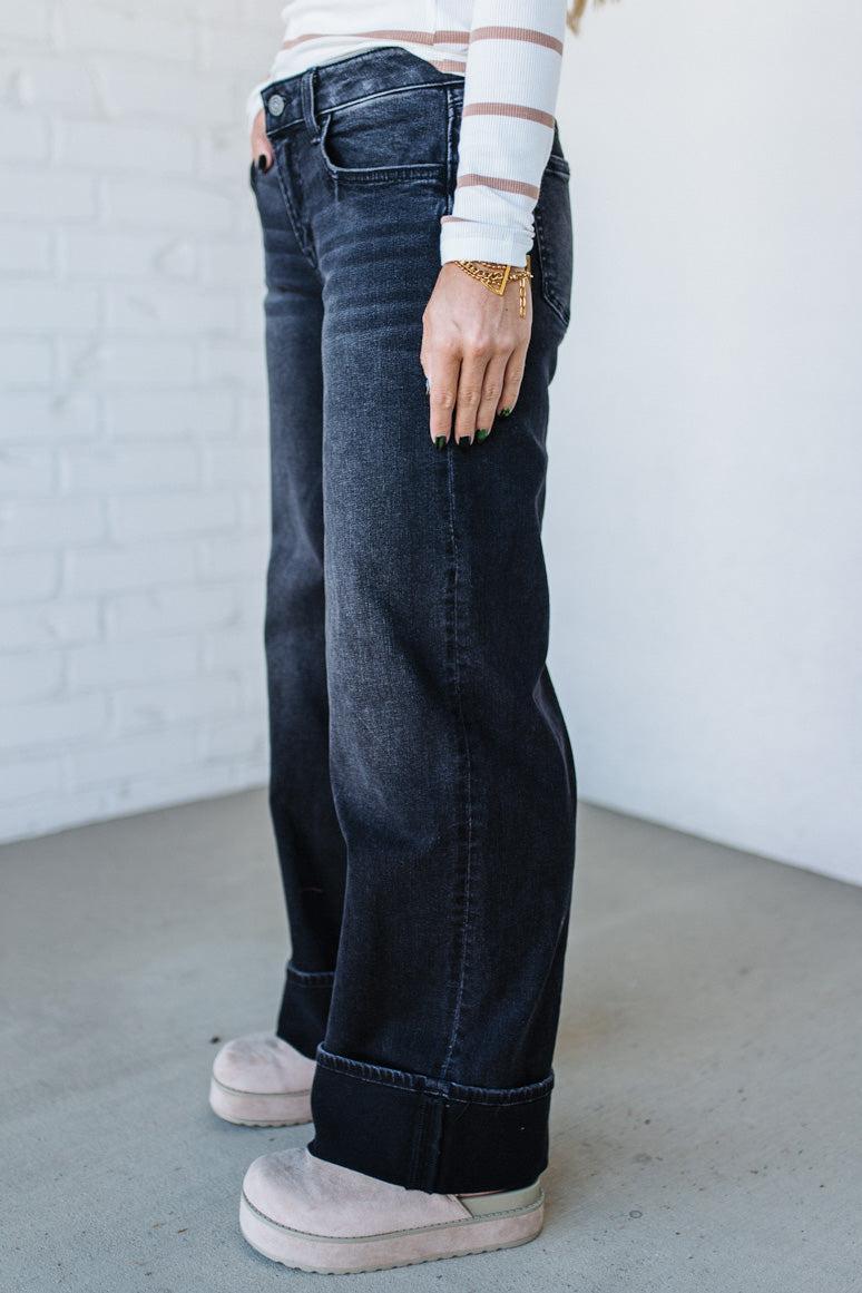 Person wearing dark blue jeans and a striped shirt against a white brick wall.
