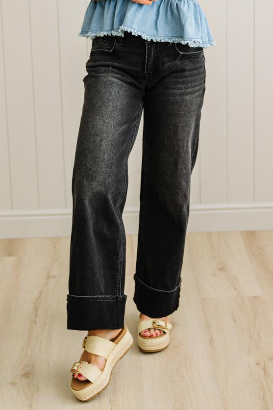 Person wearing black jeans and yellow sandals on a wooden floor.