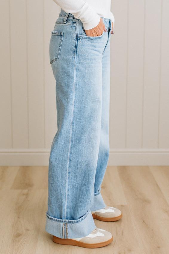 Person wearing light blue jeans and white shoes on a wooden floor with a white wall background