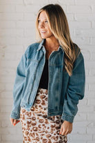Blonde woman wearing a medium wash zip front denim moto jacket.