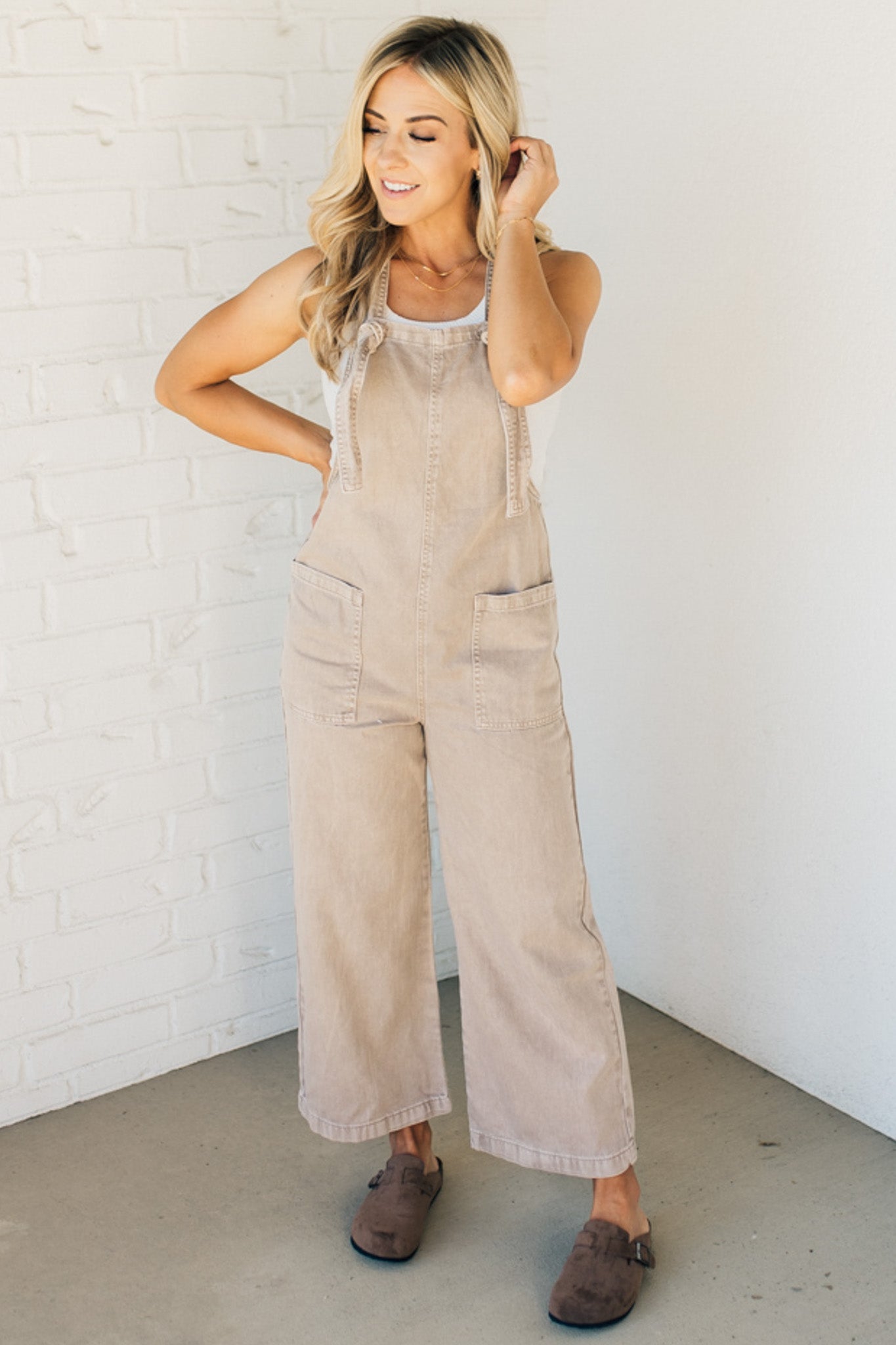Blonde woman wearing solid colored overalls with cropped wide leg and knotted strap.