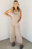 Blonde woman wearing solid colored overalls with cropped wide leg and knotted strap.
