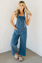 Blonde woman wearing solid colored overalls with cropped wide leg and knotted strap.