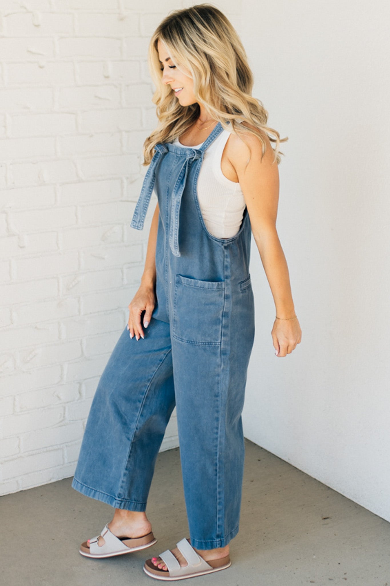 Blonde woman wearing solid colored overalls with cropped wide leg and knotted strap.
