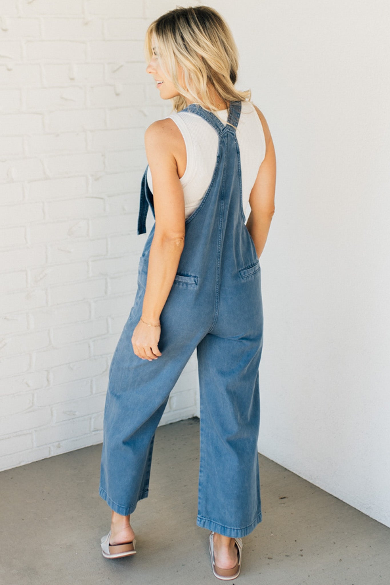 Blonde woman wearing solid colored overalls with cropped wide leg and knotted strap.