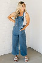 Blonde woman wearing solid colored overalls with cropped wide leg and knotted strap.