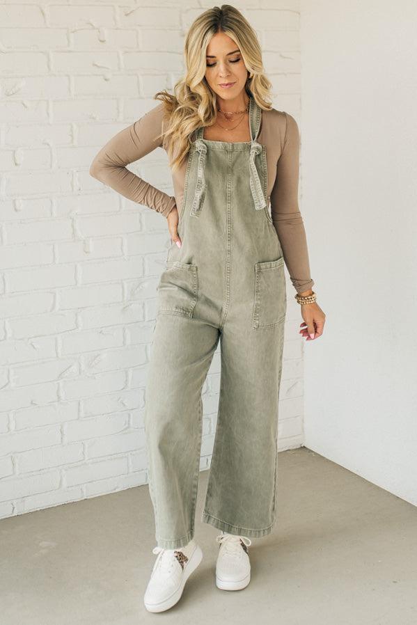 Blonde woman wearing solid colored overalls with cropped wide leg and knotted strap.