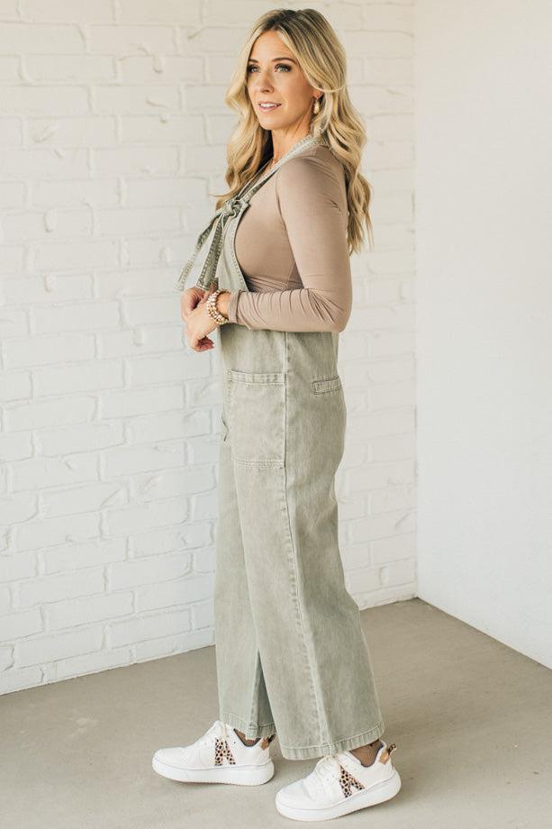 Blonde woman wearing solid colored overalls with cropped wide leg and knotted strap.