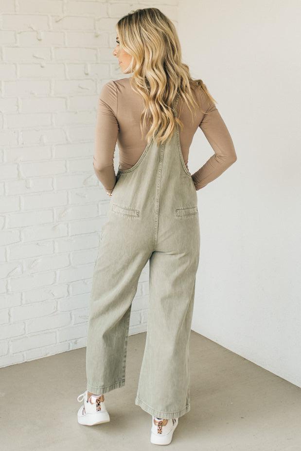 Blonde woman wearing solid colored overalls with cropped wide leg and knotted strap.