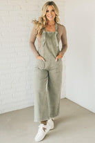 Blonde woman wearing solid colored overalls with cropped wide leg and knotted strap.