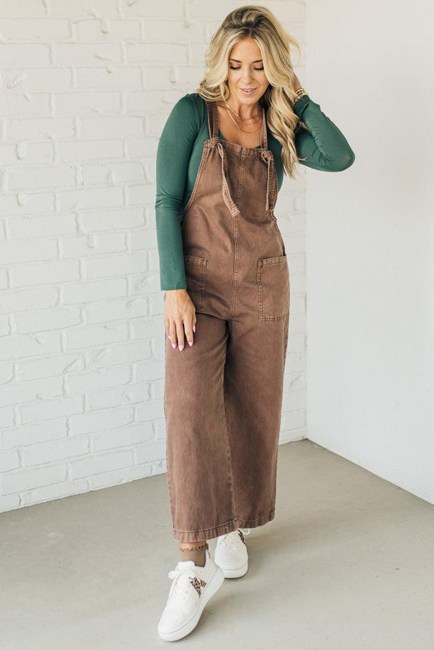 Blonde woman wearing solid colored overalls with cropped wide leg and knotted strap.