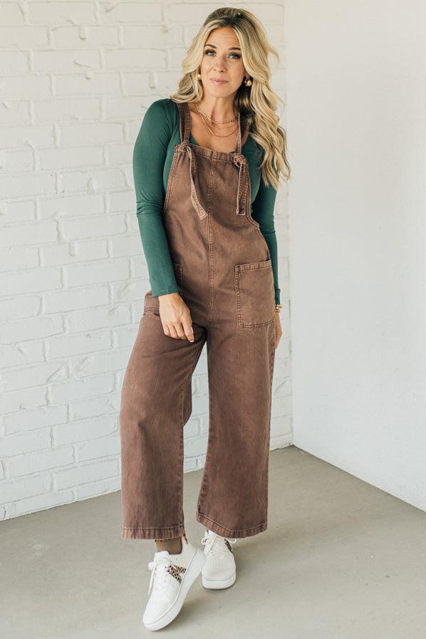 Blonde woman wearing solid colored overalls with cropped wide leg and knotted strap.
