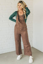 Blonde woman wearing solid colored overalls with cropped wide leg and knotted strap.