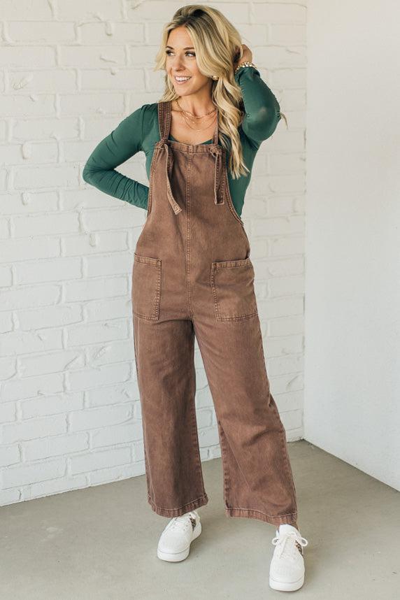 Blonde woman wearing solid colored overalls with cropped wide leg and knotted strap.
