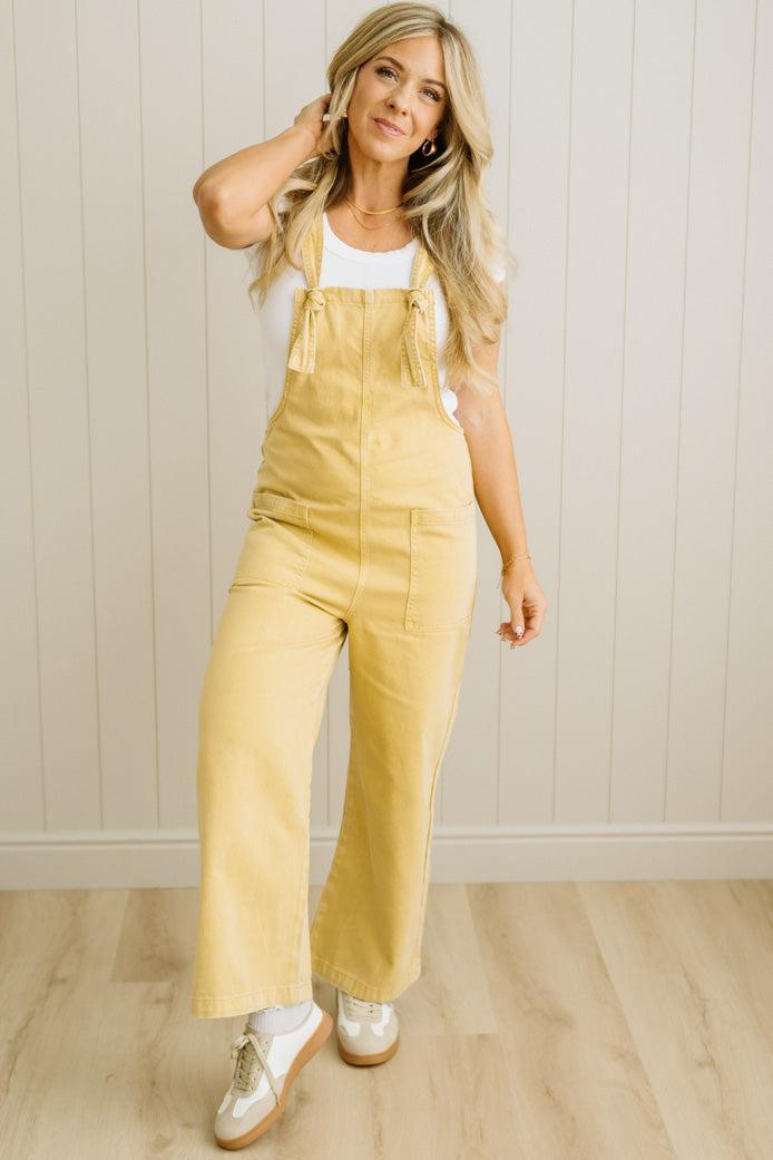 Woman wearing a yellow denim jumpsuit against a white paneled wall.