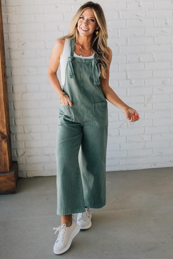 Blonde woman wearing solid colored overalls with cropped wide leg and knotted strap.