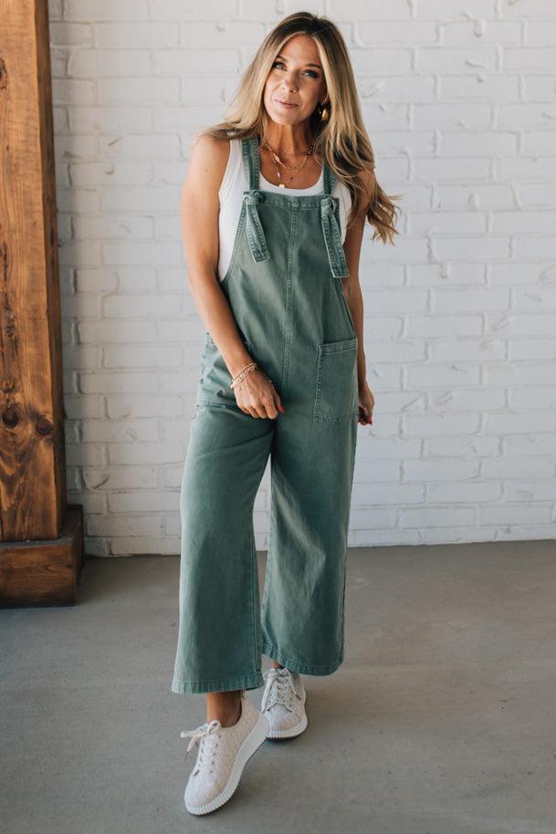 Blonde woman wearing solid colored overalls with cropped wide leg and knotted strap.