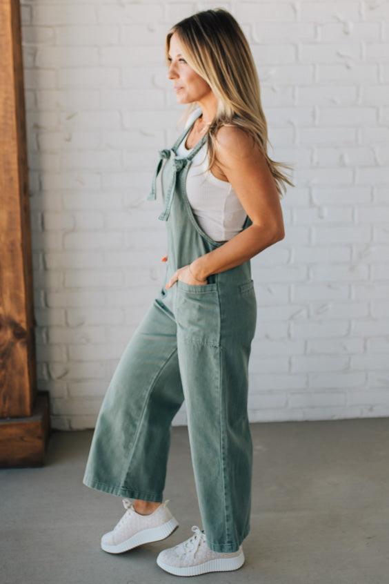 Blonde woman wearing solid colored overalls with cropped wide leg and knotted strap.