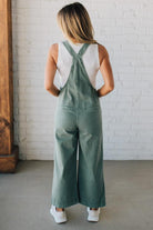 Blonde woman wearing solid colored overalls with cropped wide leg and knotted strap.