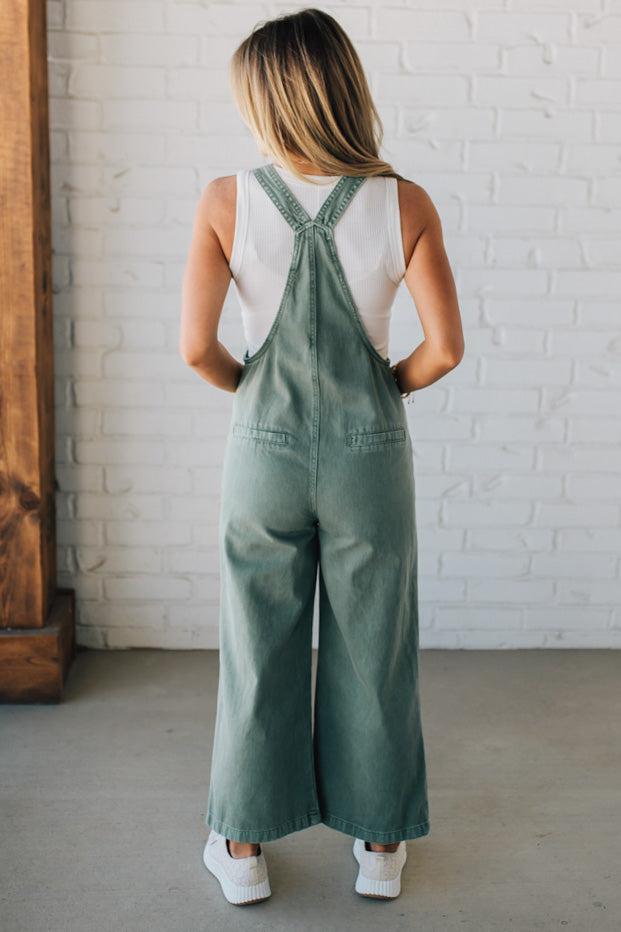 Blonde woman wearing solid colored overalls with cropped wide leg and knotted strap.