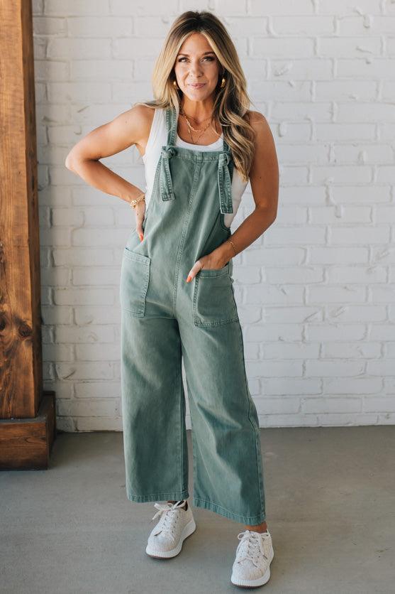 Blonde woman wearing solid colored overalls with cropped wide leg and knotted strap.