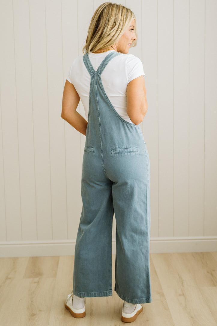 Person wearing blue denim overalls and a white shirt against a light wooden paneled wall.