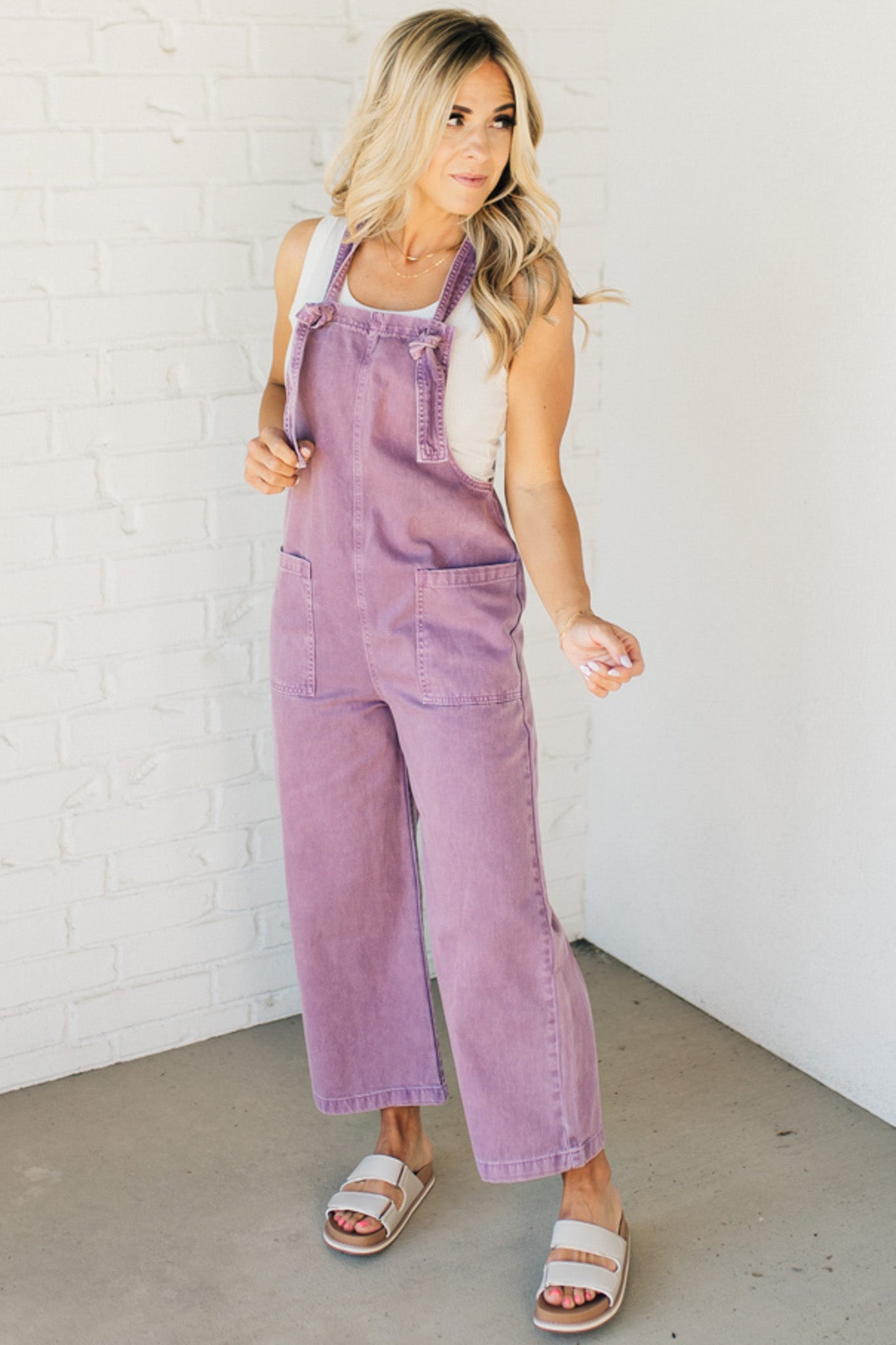 Blonde woman wearing solid colored overalls with cropped wide leg and knotted strap.