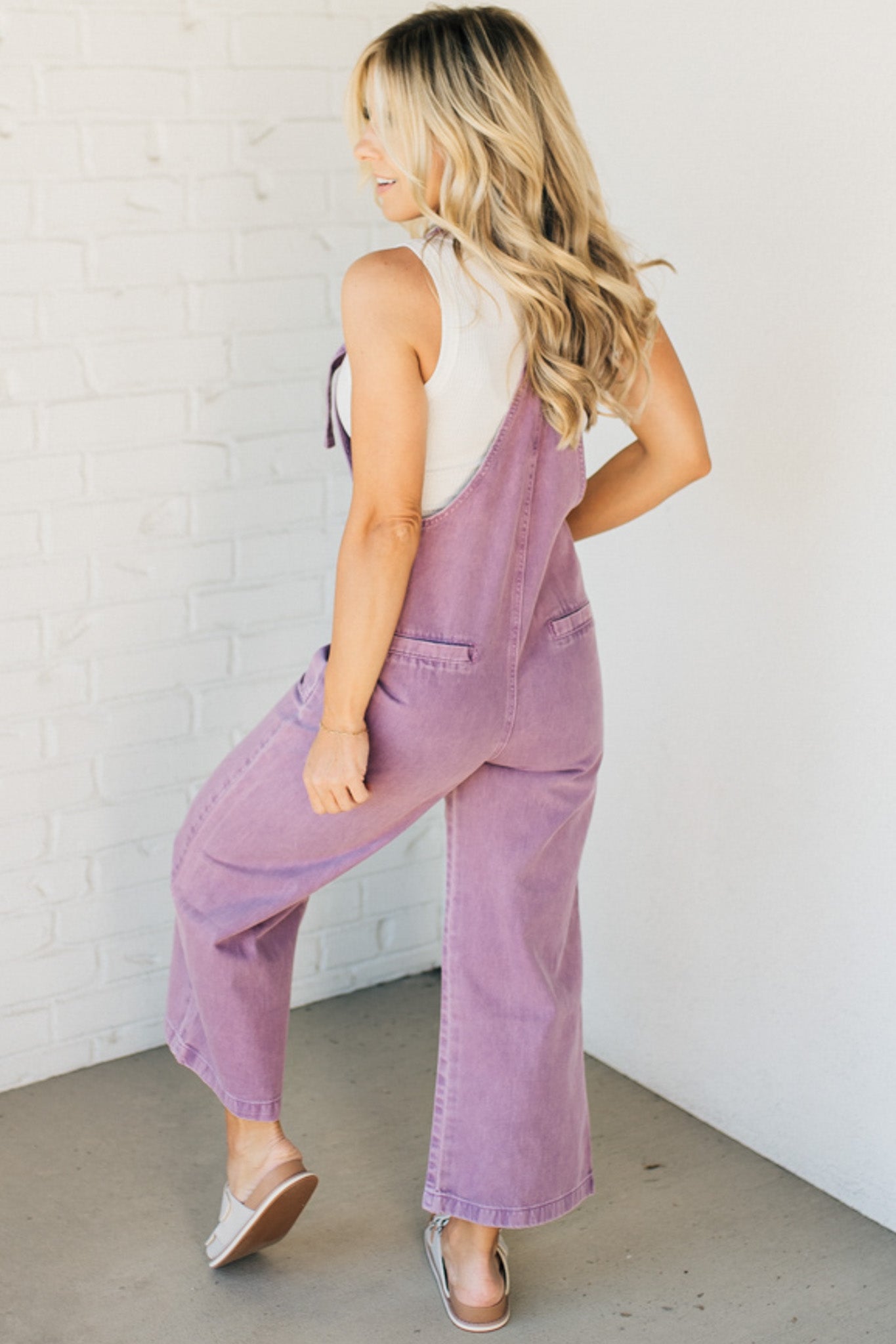 Blonde woman wearing solid colored overalls with cropped wide leg and knotted strap.