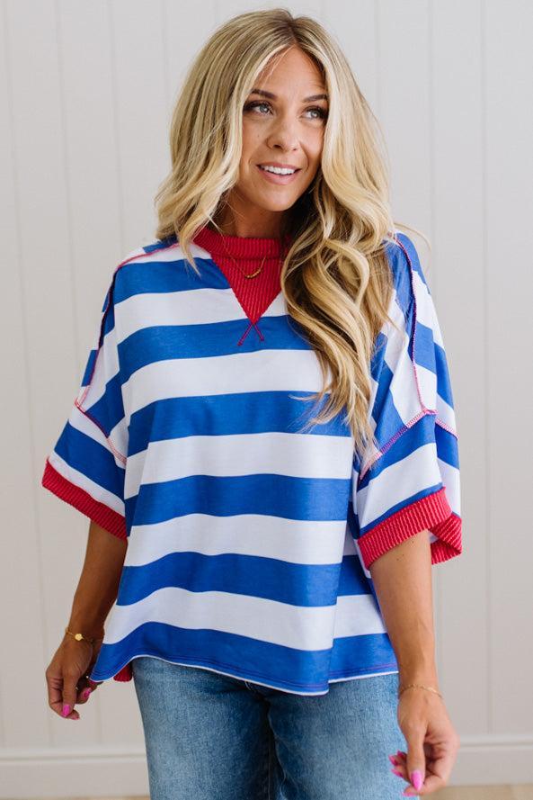 Woman wearing a blue and white striped poncho with red accents, standing against a light wooden panel background.