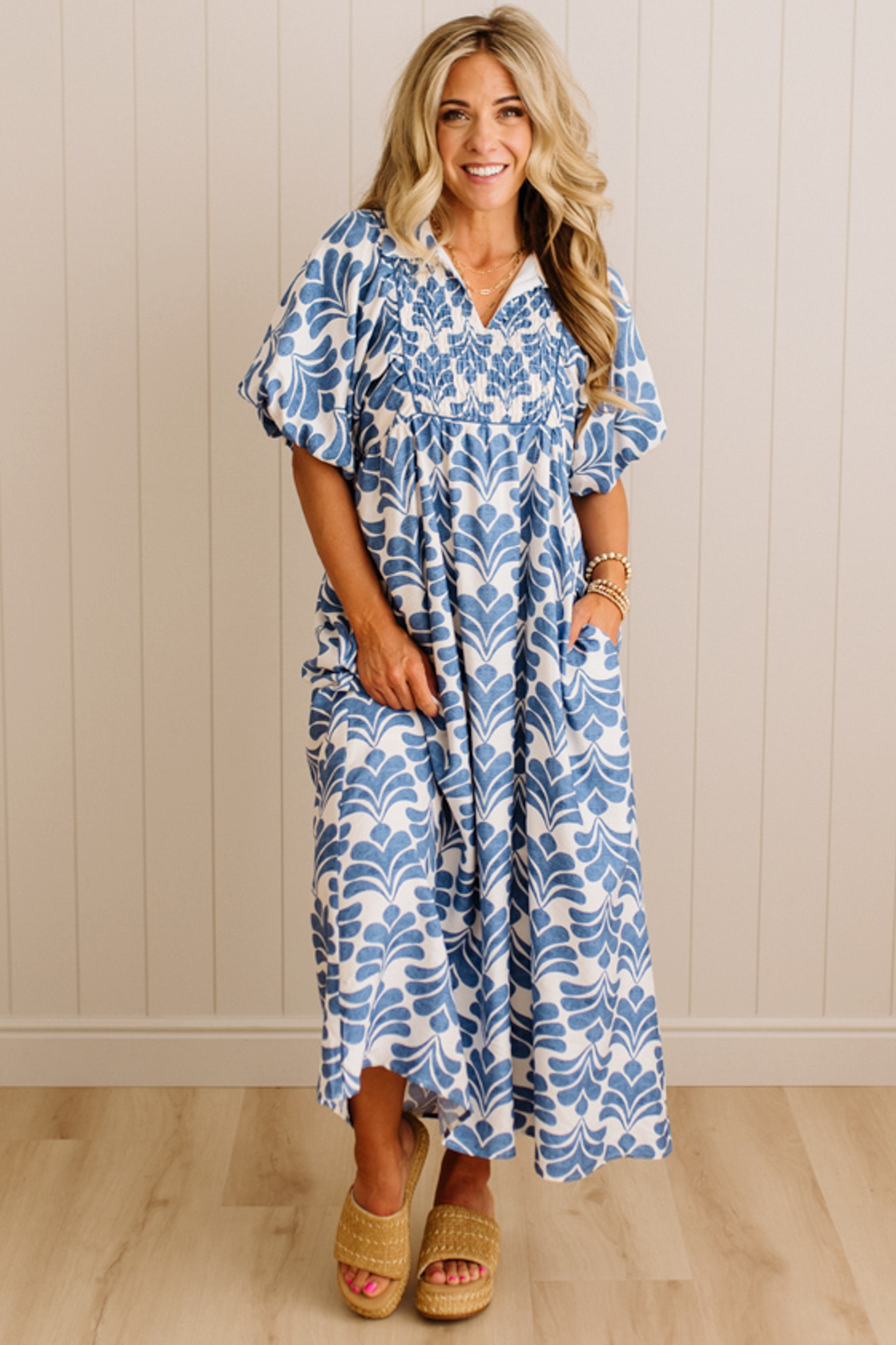 Woman wearing a blue and white patterned dress standing against a beige wall.