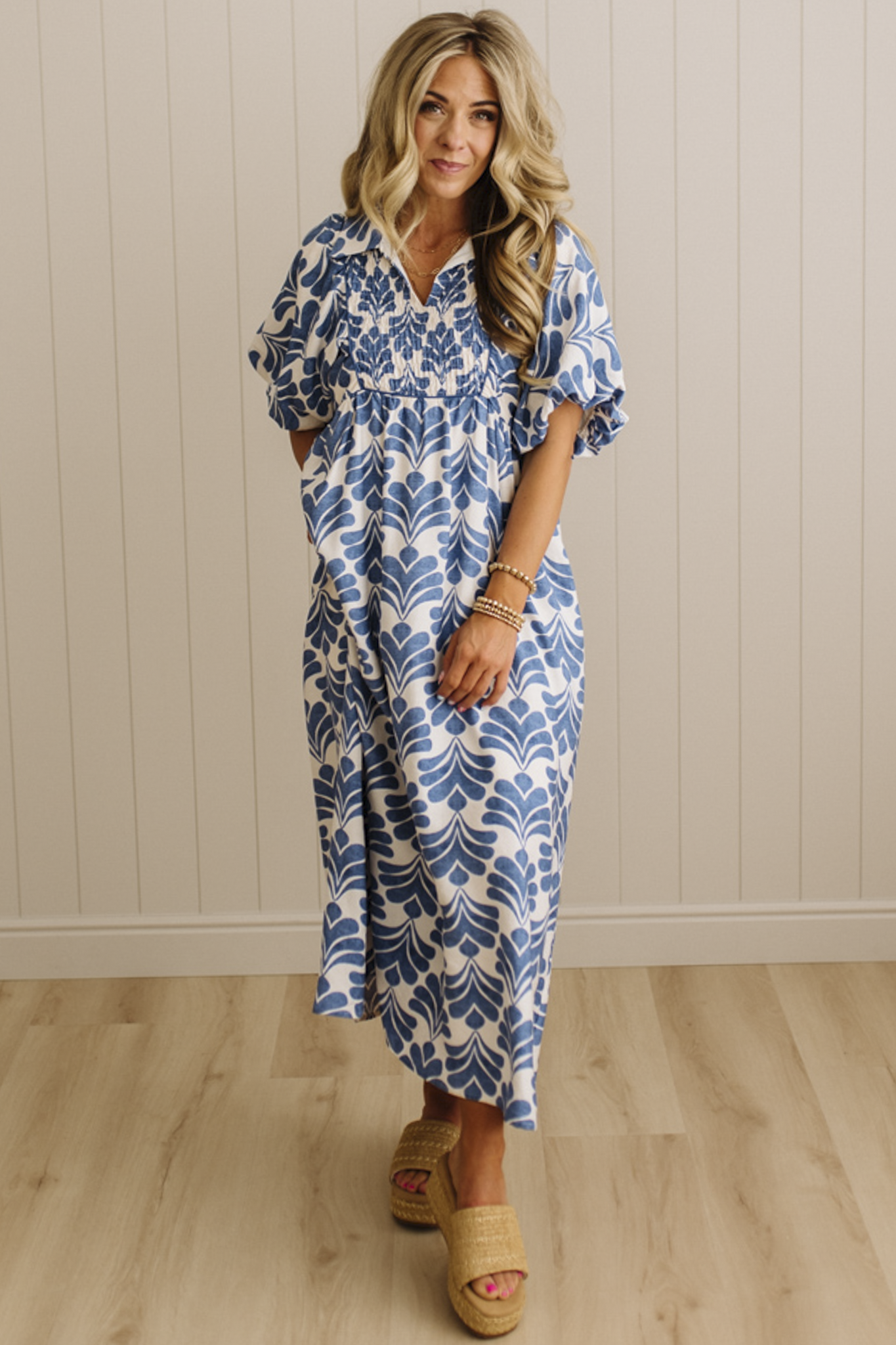 Woman wearing a blue and white patterned dress standing against a beige wall.