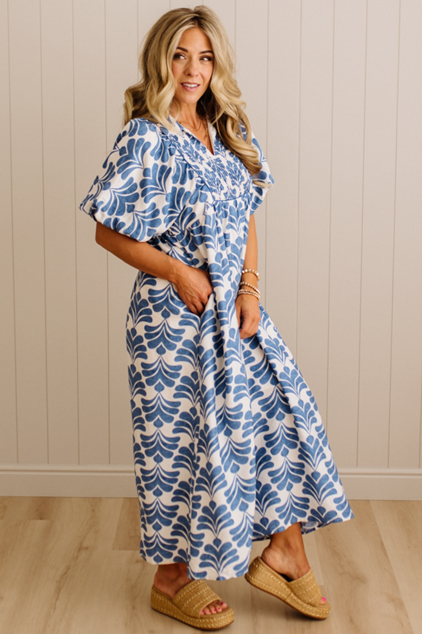 Woman wearing a blue and white patterned dress standing against a beige wall.
