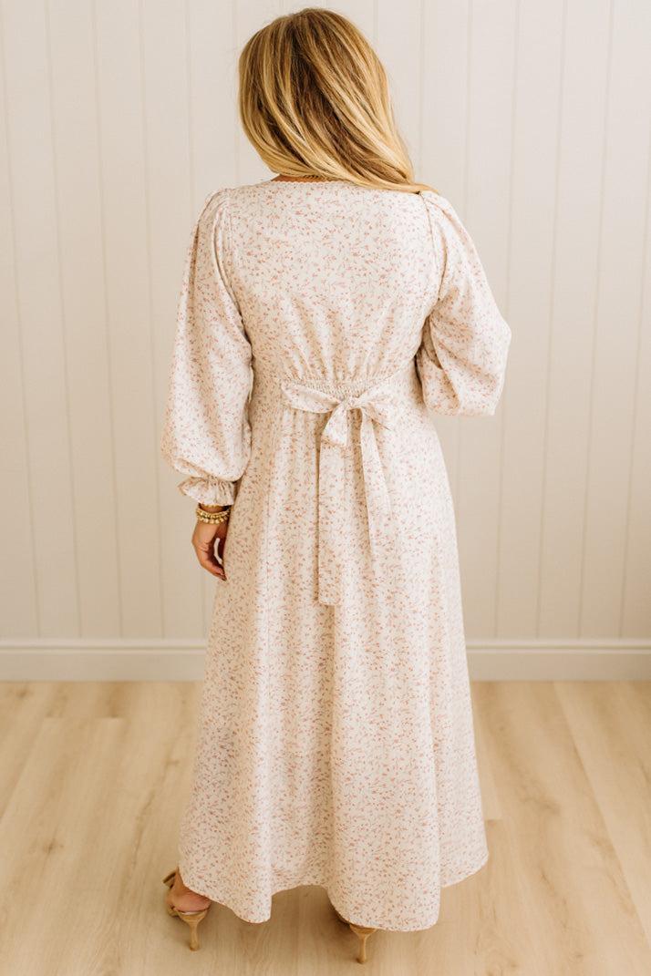 Woman wearing a long, light-colored dress with a belt against a neutral background